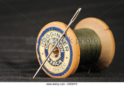 wooden-spool-of-green-sewing-thread-and-darning-needle-lying-on-black-crdep2.jpg